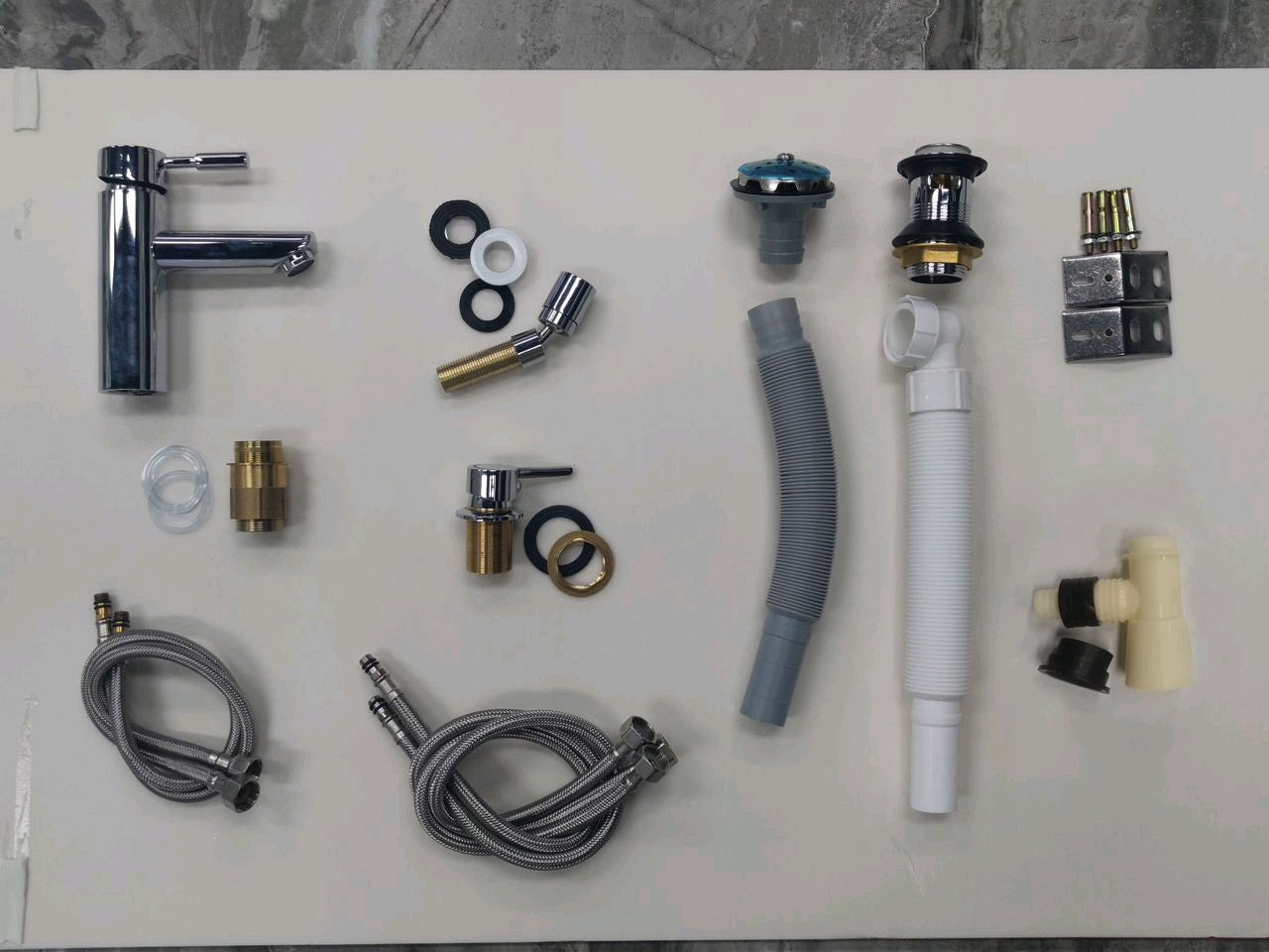 Collection of plumbing fixtures and components for Wudu ablution basin on a white surface with a gray tiled background.